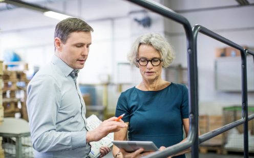 Manager with female colleague using digital tablet in printing factory. Two business people working in printing plant.